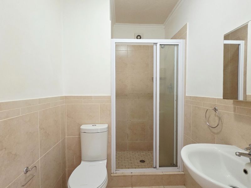 A functional bathroom featuring a shower enclosure, toilet, and washbasin with neutral wall tiling and tiled flooring.