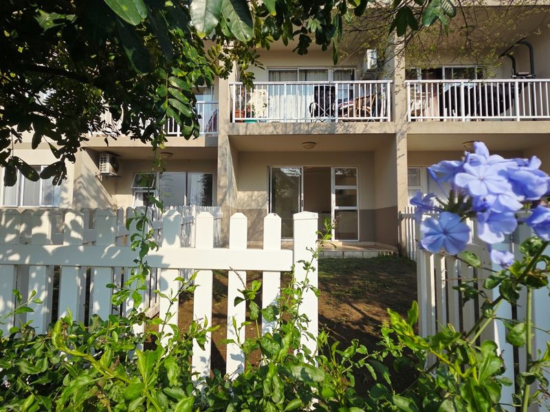 Rear view of the apartment building featuring a private garden area, white picket fencing, and upper-level balconies with sliding door access.