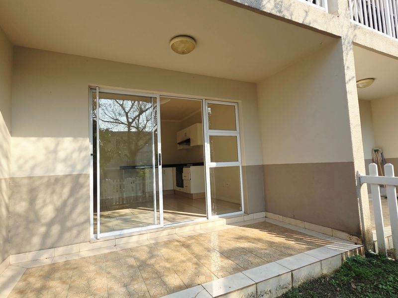 A covered ground-floor patio featuring tiled flooring, a sliding glass door entrance, and a white picket fence enclosure.