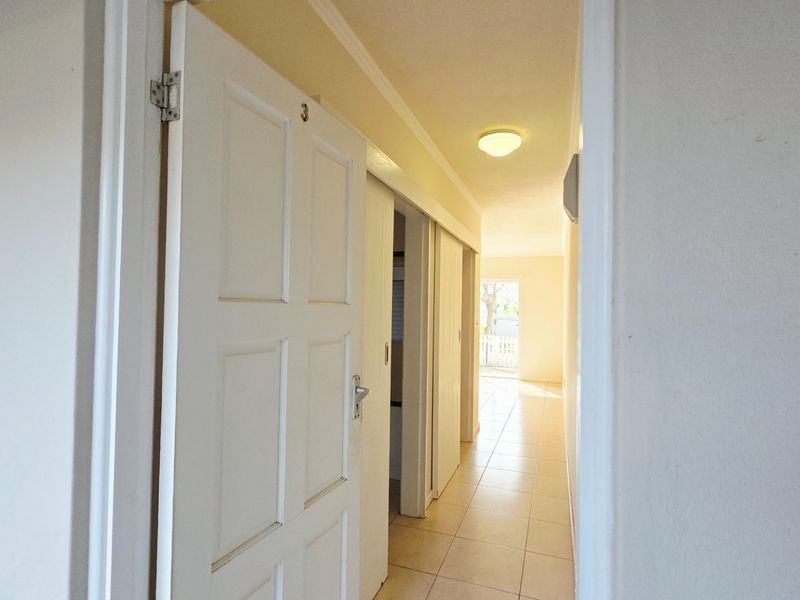 A bright, tiled hallway featuring multiple sliding doors and a standard panelled door, providing access to various rooms within the apartment.