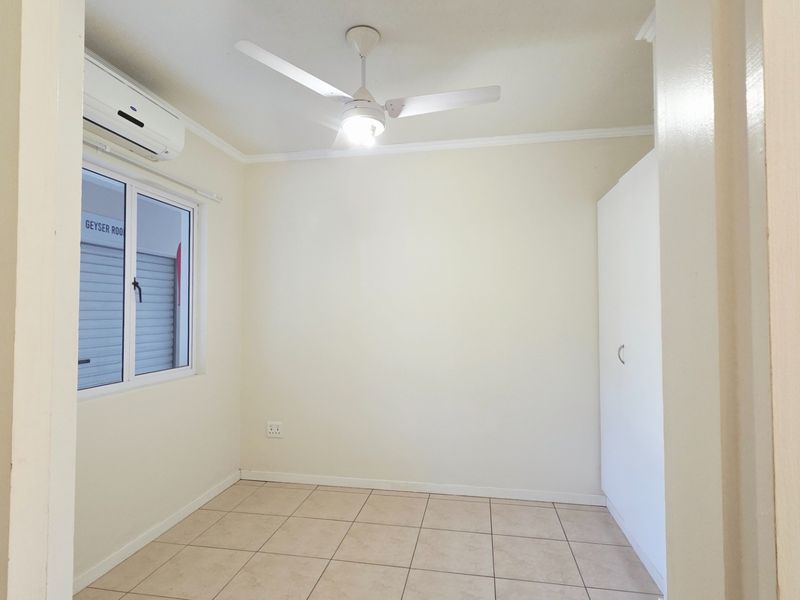 A clean, empty bedroom featuring tiled flooring, a built-in wardrobe, a ceiling fan, and an air conditioning unit.