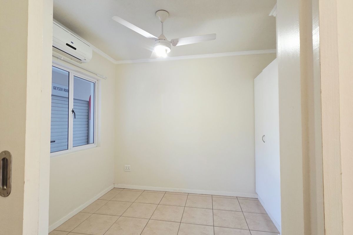A clean, empty bedroom featuring tiled flooring, a built-in wardrobe, a ceiling fan, and an air conditioning unit.