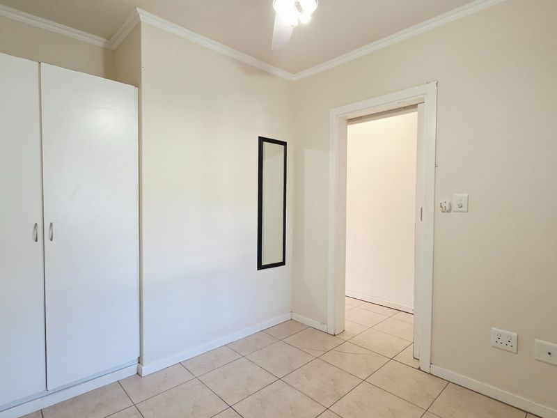 A clean, empty bedroom featuring neutral tiled flooring, a built-in wardrobe, and simple finishes, offering a blank canvas for personalization.