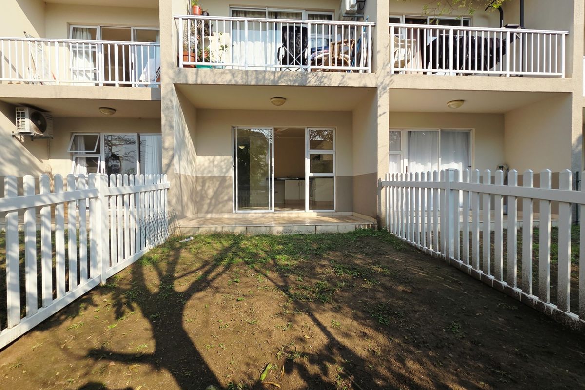 Rear view of an apartment unit featuring a private garden area with a white picket fence, covered patio, and sliding door access.