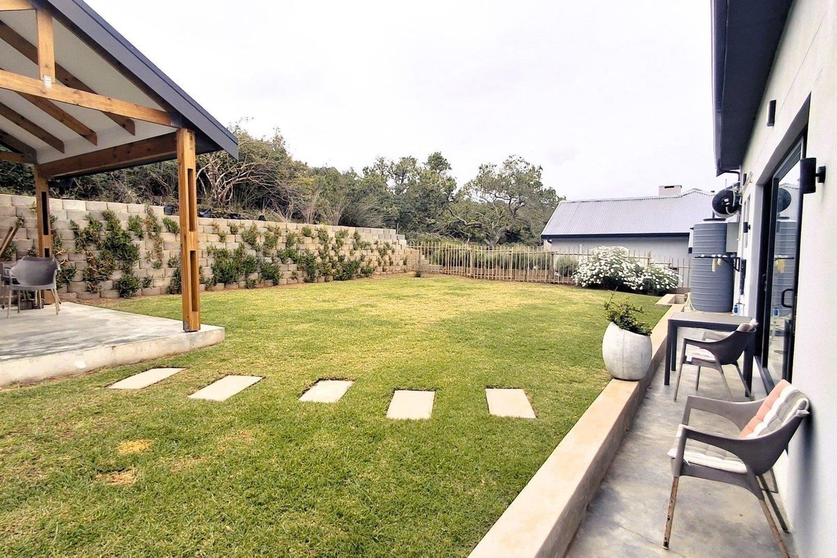 A well-maintained rear garden featuring a covered patio, lawn area, and tiered retaining wall with integrated landscaping.