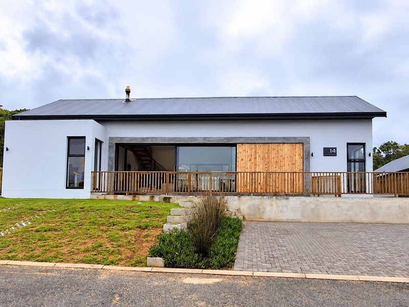 Modern single-story residence featuring a metal roof, timber sliding shutters, and a paved driveway with a landscaped front garden.