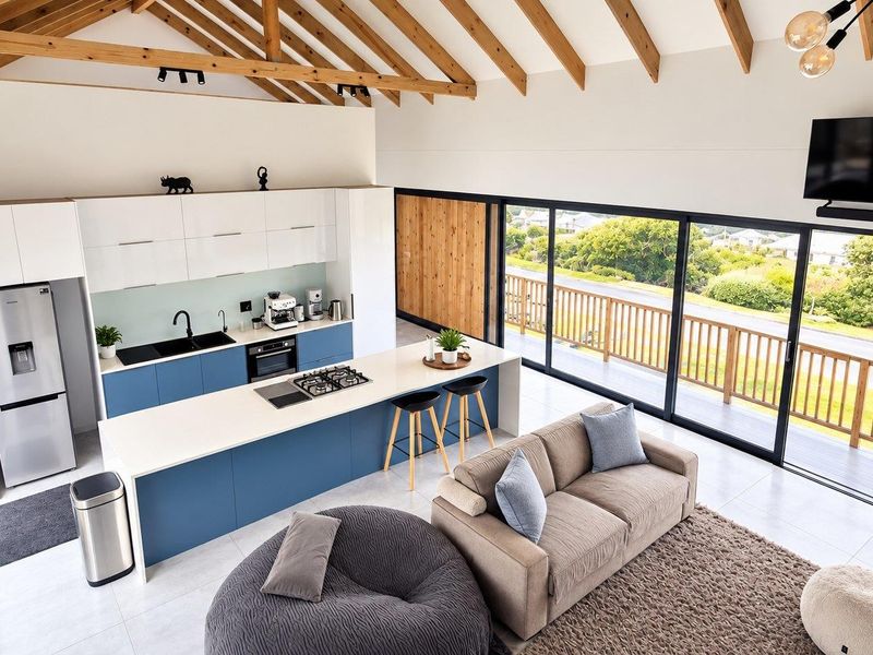 Modern open-plan living and kitchen area featuring a vaulted timber ceiling, sleek cabinetry, a central island with gas cooktop, and expansive sliding doors to deck.