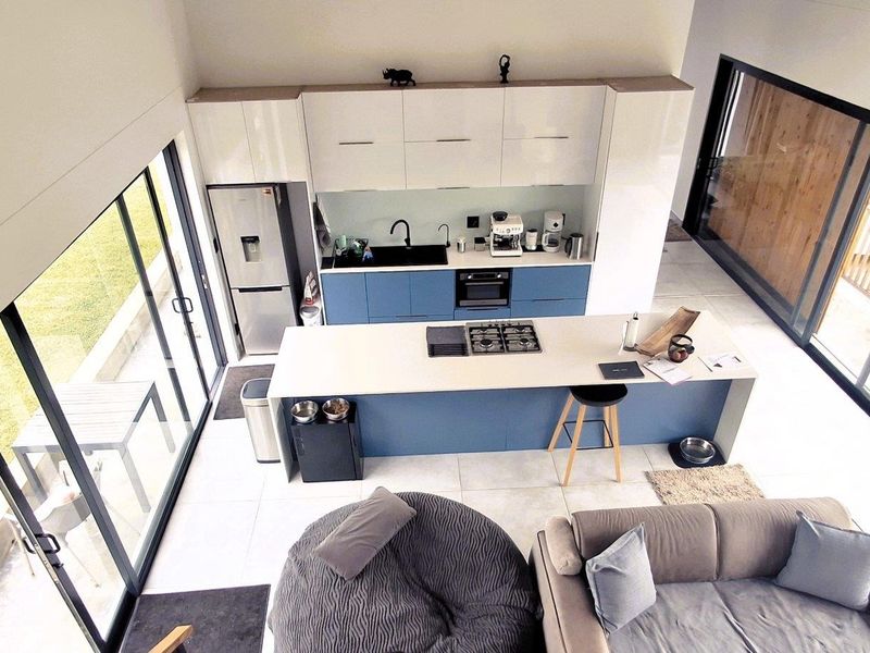 Modern open-plan living area featuring a contemporary kitchen with a central island, gas cooktop, and large sliding glass doors providing abundant natural light.