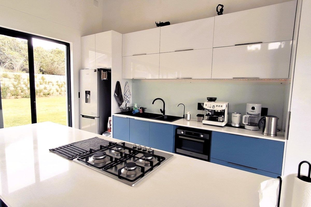Modern kitchen featuring a central island with gas hob, sleek blue and white cabinetry, quartz countertops, and direct access to the garden.