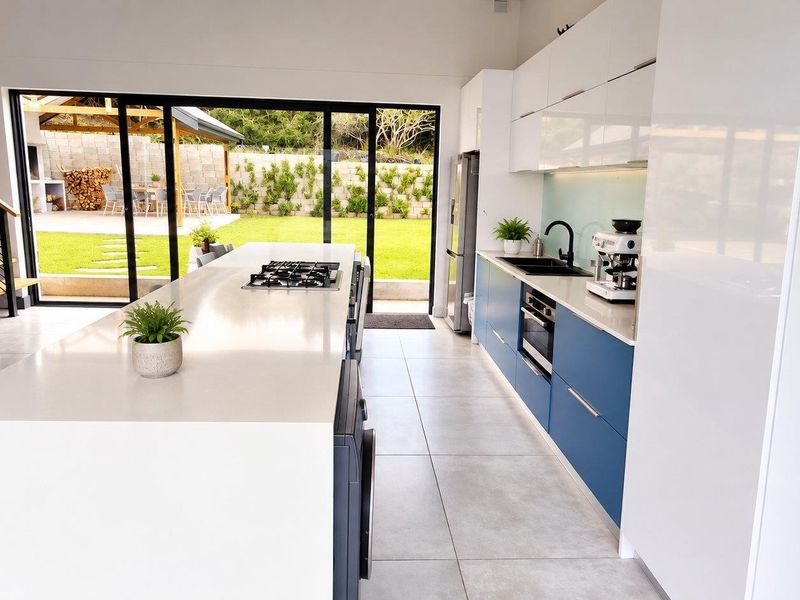 Modern open-plan kitchen featuring a large island with gas cooktop, sleek cabinetry, and seamless flow to the outdoor patio and garden area.