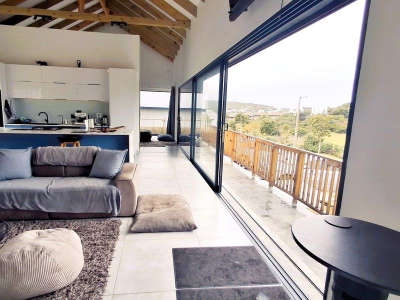 Spacious open-plan living area featuring a vaulted timber ceiling, modern kitchen with island, and large sliding doors opening onto a balcony with scenic views.