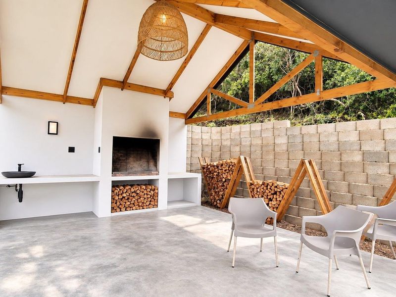 Covered outdoor patio featuring a built-in braai, concrete prep area with basin, exposed timber roof structure, and a solid concrete block retaining wall.