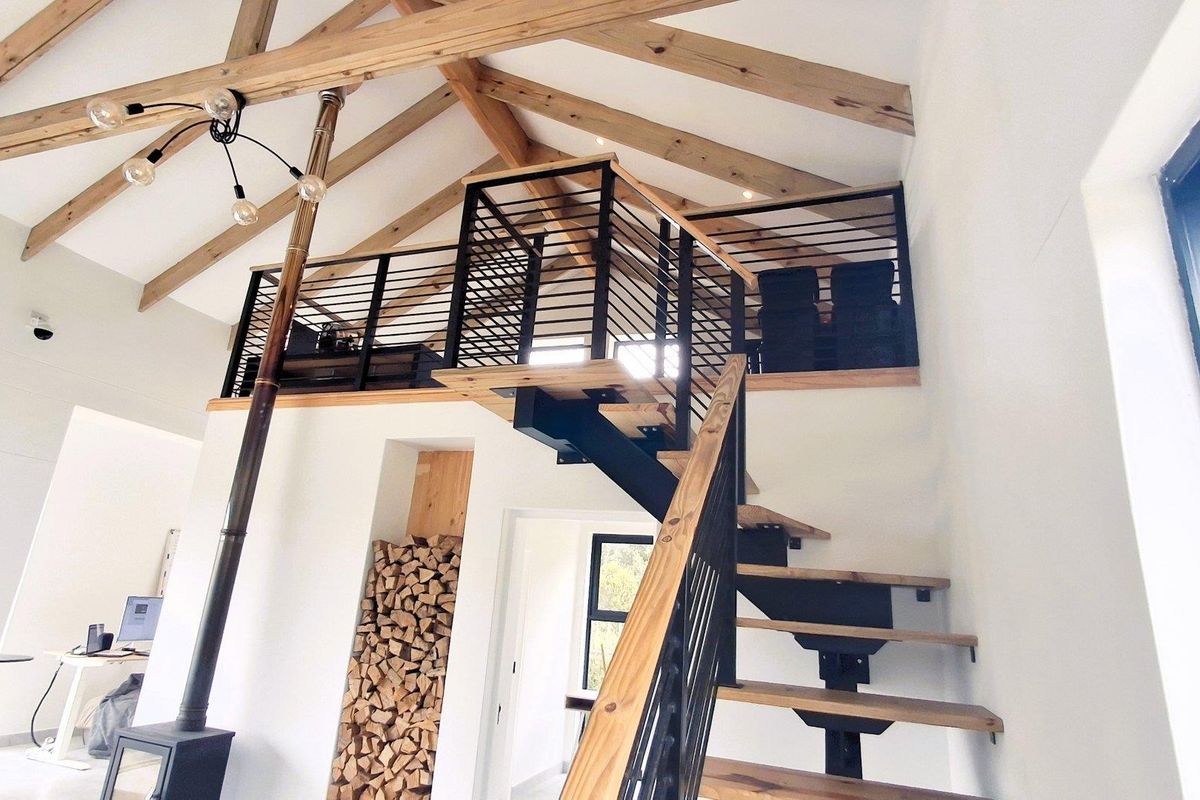 Spacious living area featuring high vaulted ceilings with exposed timber trusses, a modern mezzanine level, and a striking staircase with a built-in fireplace.
