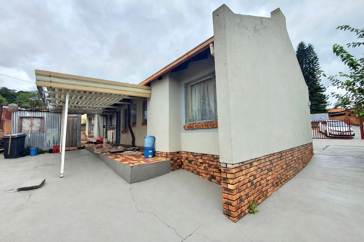Rear exterior view of the property featuring a covered patio area, concrete driveway, and brick foundation detailing.