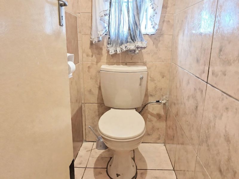 A compact bathroom featuring full-height wall tiling, a standard toilet, and a small window, presenting an opportunity for modernization.