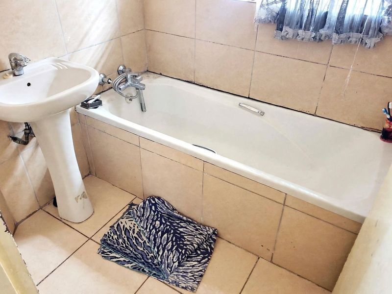 A functional bathroom featuring a pedestal basin and a built-in bathtub with tiled surrounds and flooring.