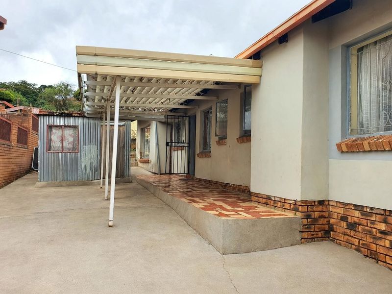 Rear exterior view featuring a covered patio area, concrete paving, and a small corrugated metal utility structure.