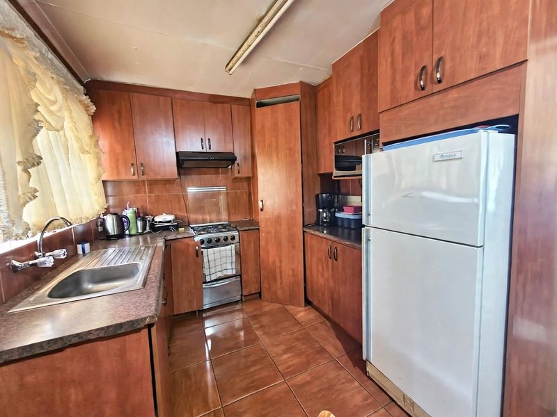 A functional kitchen featuring wood-look cabinetry, tiled flooring, a gas stove, and a stainless steel sink with ample storage space.