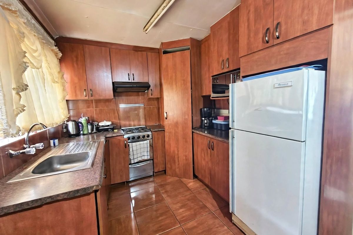 A functional kitchen featuring wood-look cabinetry, tiled flooring, a gas stove, and a stainless steel sink with ample storage space.