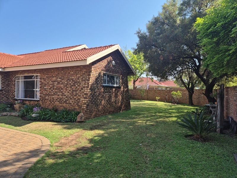 A well-maintained rear exterior view of a face brick house featuring a tiled roof, paved driveway, and a spacious landscaped garden with perimeter walling.