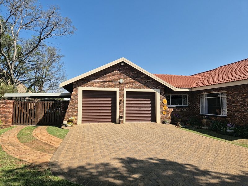 Front view of a well-maintained brick house featuring a double garage, paved driveway, and tiled roof.