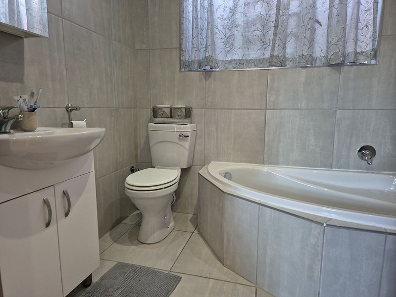 A functional bathroom featuring neutral wall and floor tiles, a corner bathtub, a vanity cabinet with a basin, and a standard toilet.