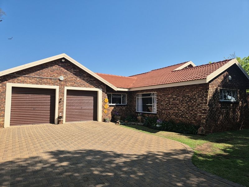 A well-maintained single-story brick house featuring a double garage, tiled roof, and a spacious paved driveway.