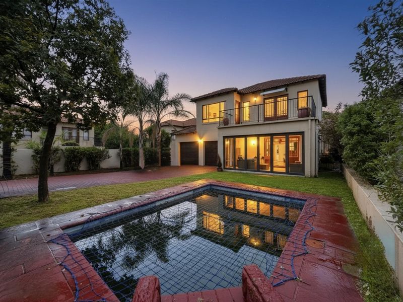 Rear view of a two-story house featuring a swimming pool with safety net, paved driveway, double garage, and an upper-level balcony.