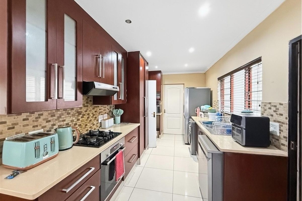 A functional kitchen featuring dark wood cabinetry, a gas hob with extractor, tiled backsplash, and light-colored tiled flooring with ample counter space.