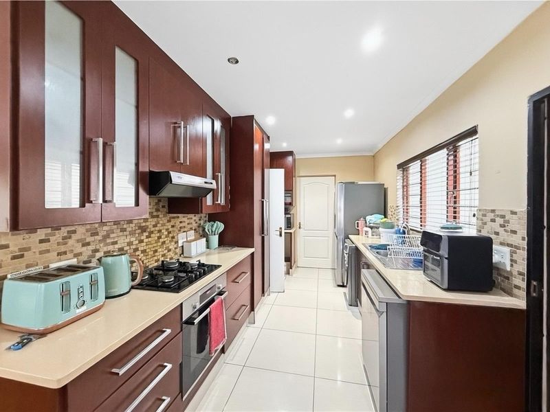 A functional kitchen featuring dark wood cabinetry, a gas hob with extractor, tiled backsplash, and light-colored tiled flooring with ample counter space.