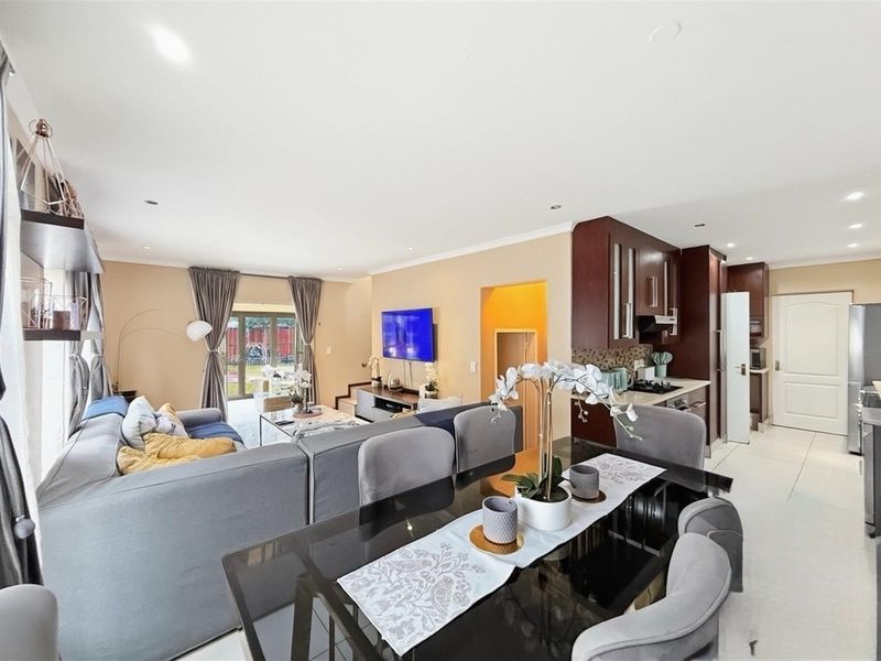 An open-plan living, dining, and kitchen area featuring tiled floors, recessed lighting, and a modern kitchen with built-in cabinetry and appliances.