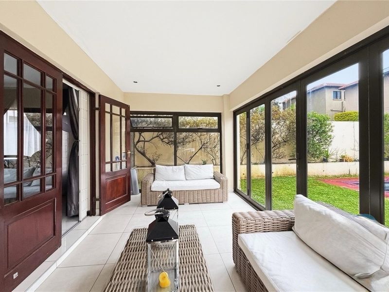 A bright, enclosed patio featuring large glass stacker doors that provide seamless access to the garden and pool area.