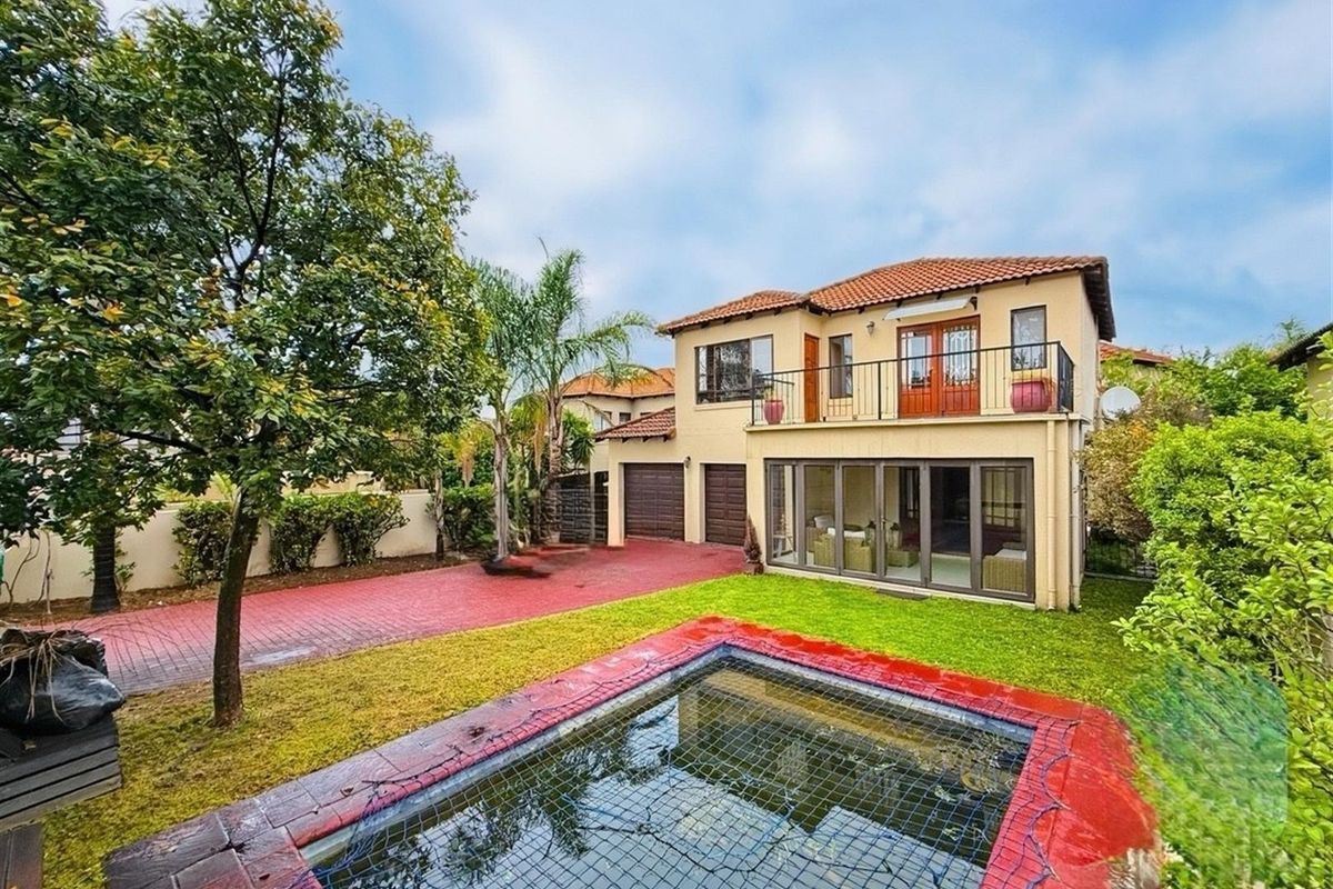 Rear view of a two-story house featuring a swimming pool, paved driveway, double garage, and an upper-level balcony with glass doors.