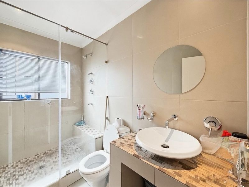Modern bathroom featuring a glass-enclosed walk-in shower with a built-in bench, a vessel sink on a tiled vanity, and neutral wall tiling.