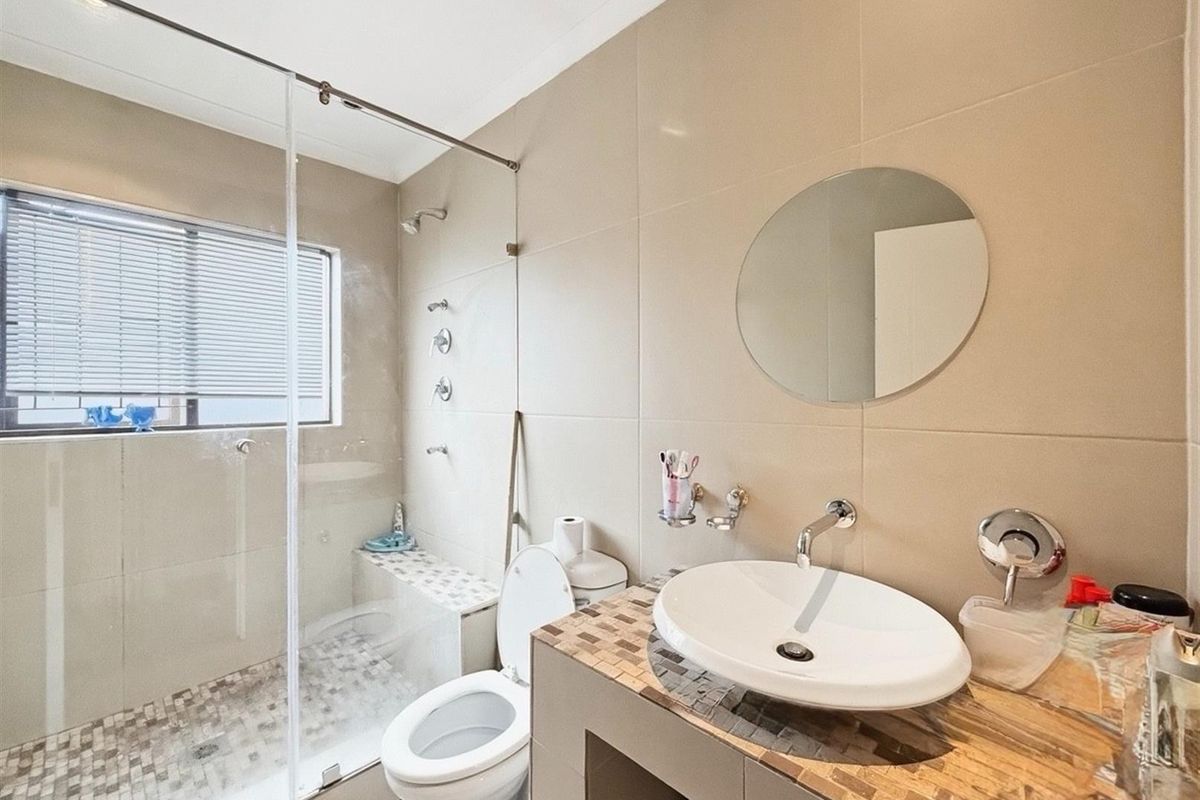 Modern bathroom featuring a glass-enclosed walk-in shower with a built-in bench, a vessel sink on a tiled vanity, and neutral wall tiling.