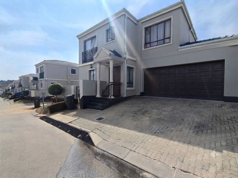Front elevation of a two-story residential house featuring a paved driveway, double garage, and a covered entrance porch with balcony above.