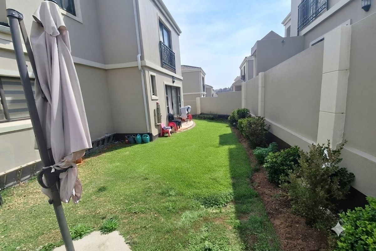 A private rear garden featuring a well-maintained lawn, boundary wall, and a paved patio area accessible via sliding glass doors.