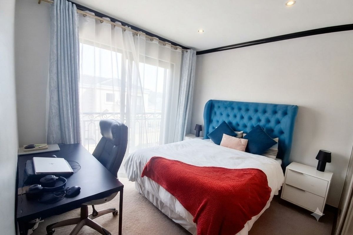 A well-lit bedroom featuring neutral carpet flooring, recessed downlights, and a sliding glass door providing access to a private balcony.