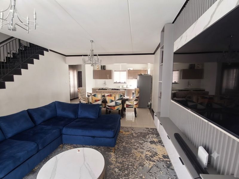 Spacious open-plan living and dining area featuring modern built-in cabinetry, tiled flooring, and a staircase, seamlessly connecting to the kitchen space.