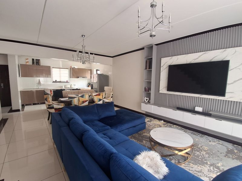 Modern open-plan living area featuring a sleek kitchen with built-in cabinetry and a contemporary media wall with integrated shelving and lighting.