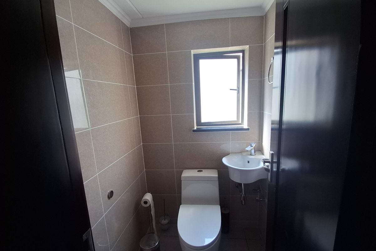 A compact, modern guest bathroom featuring neutral wall tiles, a sleek toilet, and a wall-mounted basin.