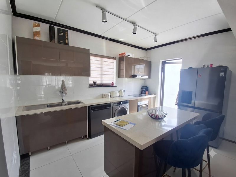 Modern kitchen featuring glossy cabinetry, stone countertops, integrated appliances, and a central island with breakfast bar seating, complemented by sleek tiled flooring.