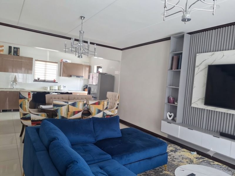 Spacious open-plan living area featuring a modern kitchen with built-in cabinetry and a contemporary media wall unit with integrated shelving.