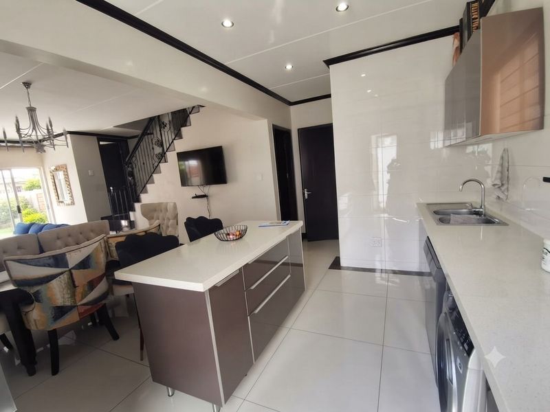 Modern open-plan kitchen and living area featuring a central island, sleek cabinetry, quartz countertops, and a staircase leading to the upper level.