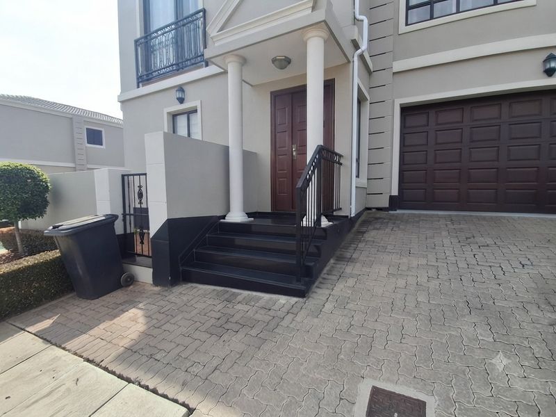 Front elevation of a multi-story house featuring a paved driveway, double garage, and a covered entrance with decorative columns and stone steps.