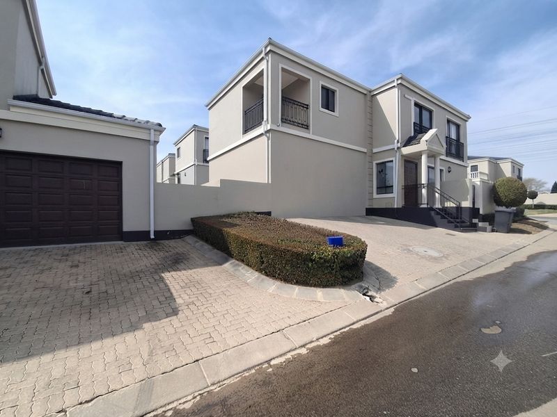 Front elevation of a modern double-story townhouse featuring a paved driveway, single garage, and an upper-level balcony with wrought iron railings.