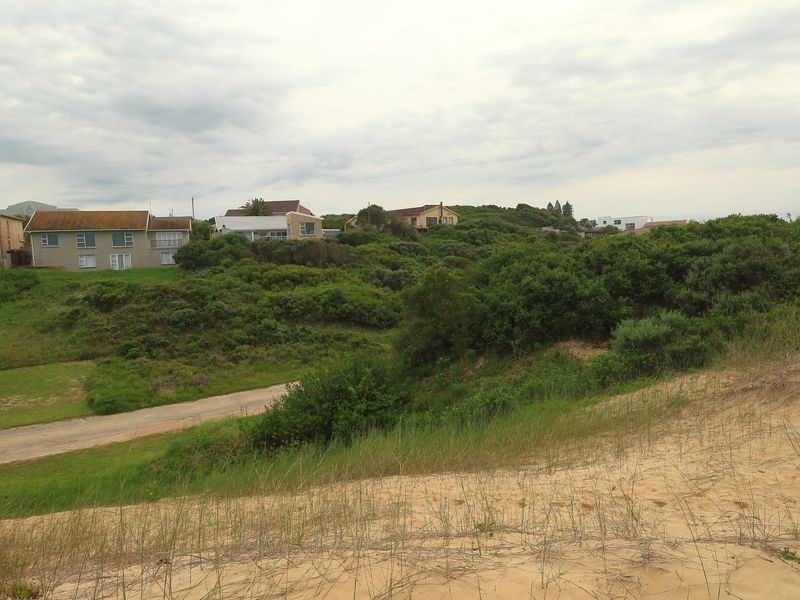 A scenic view of the vacant residential land featuring natural sand dunes, coastal vegetation, and an unpaved access road with surrounding residential properties.