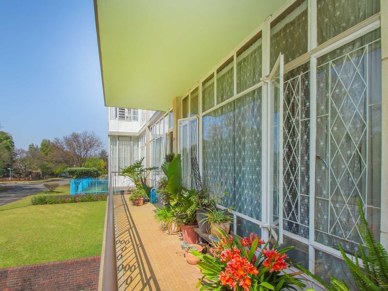 A spacious apartment balcony featuring tiled flooring, metal security bars on windows, and a metal railing overlooking the surrounding garden area.