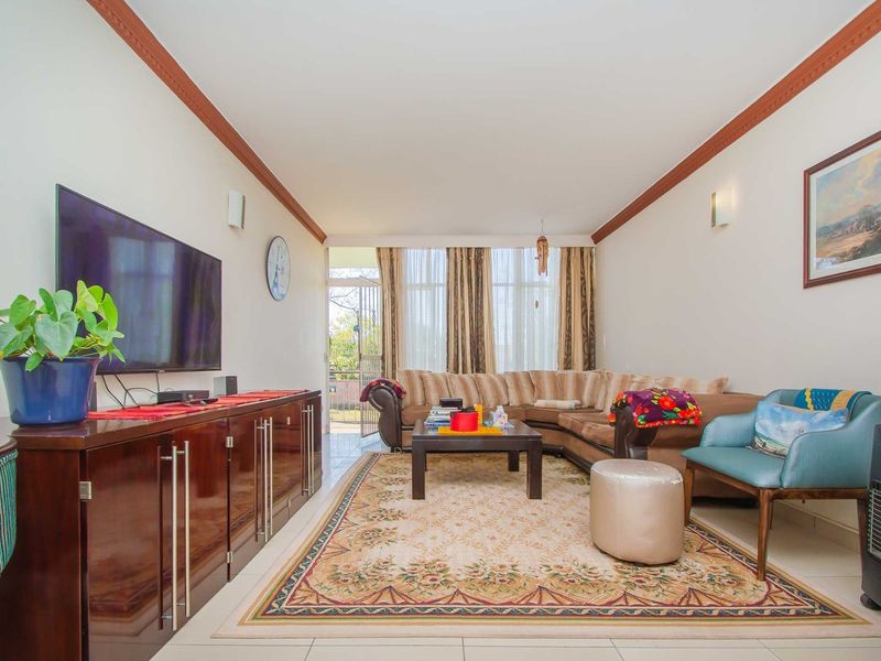 A spacious living room featuring tiled flooring, crown molding, and direct access to an outdoor patio area through a sliding glass door.