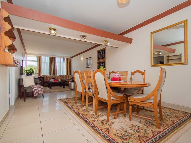 Spacious open-plan living and dining area featuring tiled flooring, exposed ceiling beams, and large windows providing ample natural light.